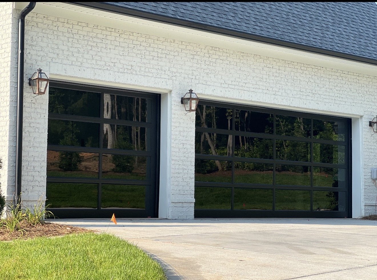 Two black full-view glass garage doors with divided lites on a white painted brick home